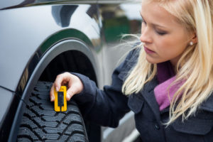 a young woman is measuring the tread depth of her car tire. the proper depth in the tread of a tire can prevent accidents.